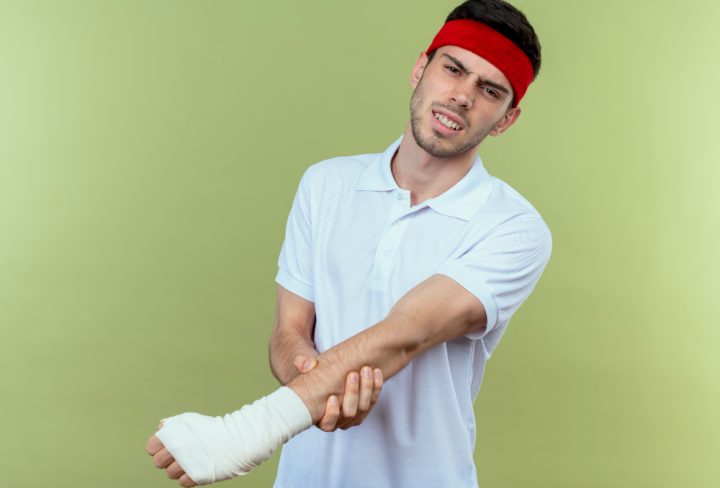 young-sporty-man-headband-touching-his-bandaged-hand-feeling-pain-standing-green-background